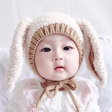 Close-up of cozy beige baby knit hat with long rabbit ears and warm chin strap ties