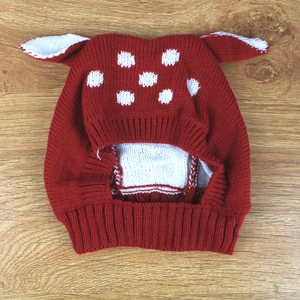 Detailed close-up of a red and white polka dot knit hat with cute 3D ears on wood background