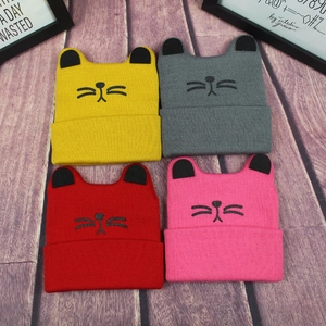 Detailed view of four colorful knitted cat ear beanies in yellow, grey, red and pink