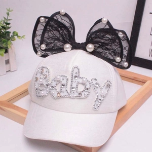 Dettaglio cappello bambina con fiocco in pizzo, perle e scritte Baby in strass lucidi