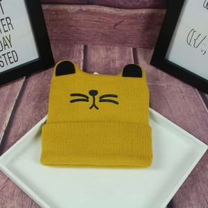 Detail of a bright yellow knitted baby hat with cat ears and embroidered face features