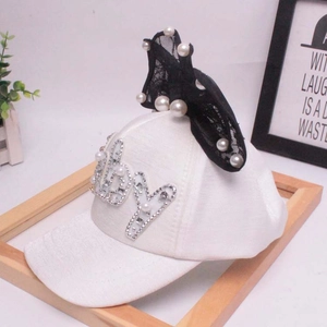 Dettaglio cappello bianco con lettere di perle e grande fiocco in pizzo a pois neri