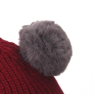 Close-up of deep red knit hat with a fluffy grey faux fur pompom detail