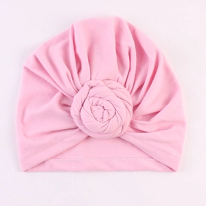 Détail d'un bonnet turban rose orné d'une grande fleur de rose faite à la main