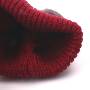 Detailed close-up of dark red knitted baby hat with soft grey pompom and ribbed texture