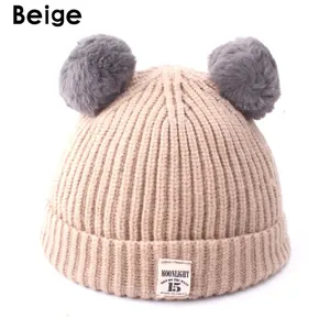 Detail of beige knit baby hat featuring grey faux fur pompoms and Moonlight woven label