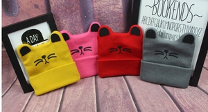Flat lay of colorful knitted kids cat ear beanies in yellow, pink, red and dark grey