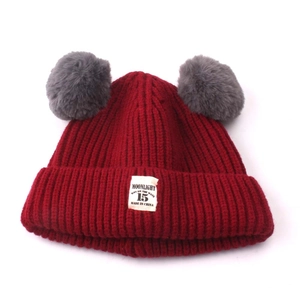 Detail of red knitted baby hat featuring double grey pom-poms and moonlight fabric label