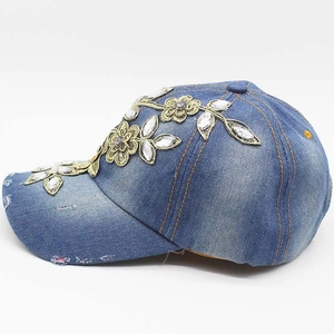 Detail view of denim baseball cap featuring gold lace flowers and rhinestone embellishments