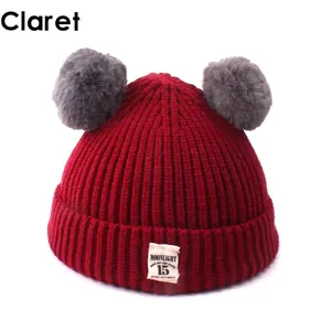 Winter knit baby beanie in claret red with double grey faux fur pom poms and label