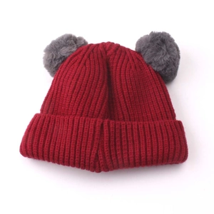 Detail of red ribbed knit baby hat featuring grey faux fur pompoms and folded brim
