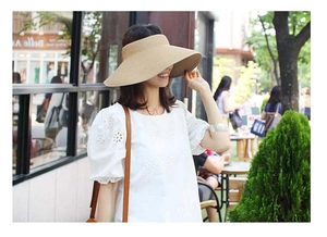 Outdoor street photo of a woman wearing a khaki wide-brim straw sun hat with an open-top