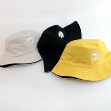 Detailed close-up of small daisy embroidery on beige, black and yellow bucket hats