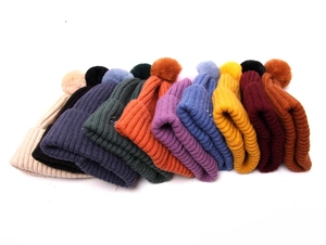Vue détaillée de bonnets d'hiver tricotés en dix couleurs avec pompons en fausse fourrure