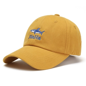 Close-up of mustard yellow cotton baseball cap with blue shark and HaHa embroidery