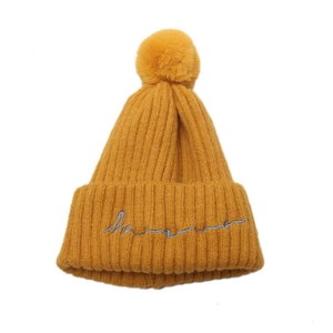 Détail du bonnet en tricot côtelé jaune gingembre avec broderie bleue et pompon décoratif