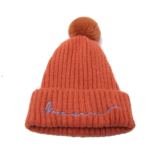 Détail du bonnet en maille orange avec pompon et broderie cursive bleue élégante