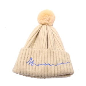 Détail d'un bonnet en maille côtelée blanc cassé avec pompon jaune et broderie bleue