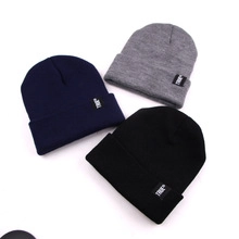 Detail view of navy, grey, and black cuffed beanies with American flag style and woven labels