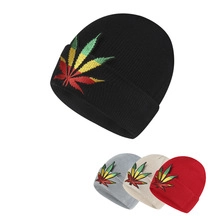 Detail of multi-color knit beanies featuring cannabis leaf embroidery in reggae colors