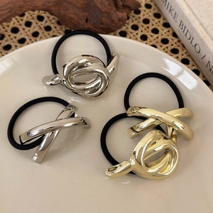 Minimalistische Haargummis mit Metallknoten in Gold und Silber auf einem weißen Teller