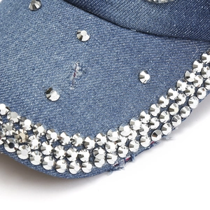 Détail d'une casquette de baseball en jean bleu avec strass argentés et texture délavée