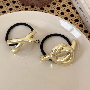Nahaufnahme von goldenen Metallknoten-Haargummis auf einem ästhetischen weißen Keramikteller