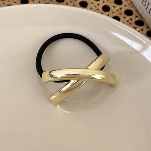 Detailaufnahme der X-förmigen goldenen Metallschließe an einem schwarzen Haargummi