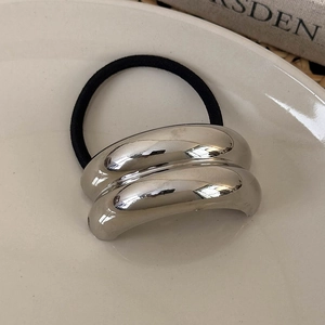 Minimalist silver metal hair tie with curved geometric design on ceramic plate