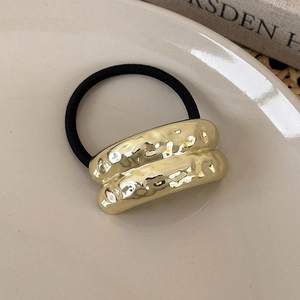 Close-up of golden geometric metal hair tie with irregular hammer texture on cream plate
