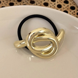 Nahaufnahme des goldenen Metall-Haargummis auf einem weißen Teller mit Weidenmatte