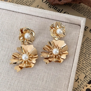 Detail of gold flower earrings with pearls on a rustic background with linen texture
