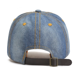 Dettaglio del cappellino in denim blu con cuciture gialle e chiusura in cinturino pelle