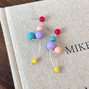 Détail de boucles d'oreilles pendantes en résine colorée sur une surface en lin