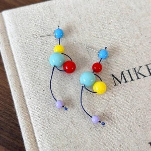 Détail de boucles d'oreilles pendantes asymétriques avec boules de résine colorées