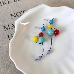 Détail de boucles d'oreilles en résine colorée avec perles rouges, jaunes et bleues