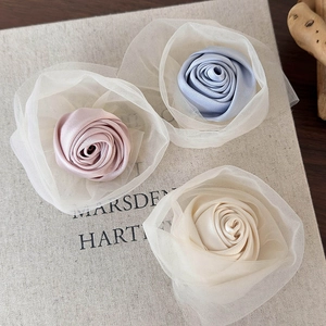 Nahaufnahme von rosa, blauen und beigen Satin-Rosen-Haarspangen mit feinen Tüllschichten