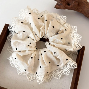 Dettaglio elastico scrunchie crema a pois con pizzo su vassoio di legno