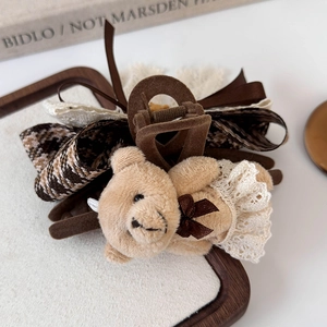 Close-up of plush teddy bear hair claw clip with lace skirt and brown checkered ribbons