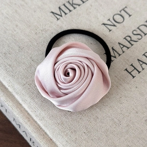 Detail eines eleganten Haargummis mit blassrosa Satinrose und schwarzem Gummiband