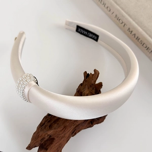 Detail view of thickened cream satin headband with neat rows of small pearls on wooden stand