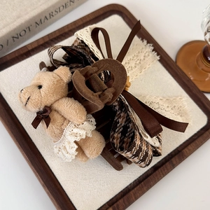 Close-up of brown hair claw clip featuring a plush bear with lace dress and plaid ribbon