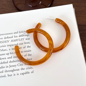 Dettaglio di orecchini a cerchio a C in resina ambrata con texture tartarugata su libro