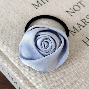 Detailansicht eines hellblauen Satin-Rosen-Haargummis auf einem Buch mit feiner Textur