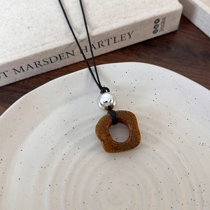 Artistic camel bone pendant necklace with polished silver bead on white ceramic tray