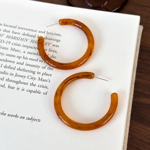 Dettaglio di grandi orecchini a cerchio in resina ambrata su una pagina di libro