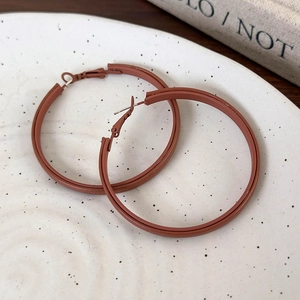 Macro shot of large double-layer brick red matte leather hoops on ceramic tray