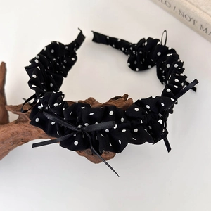 Detailed close-up of a black and white polka dot headband with sweet bow on wood branch