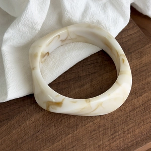Detail of chunky resin bangle with cream and brown marble pattern on wooden surface