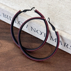 Macro detail of large hoop earrings featuring burgundy faux leather texture and black accents